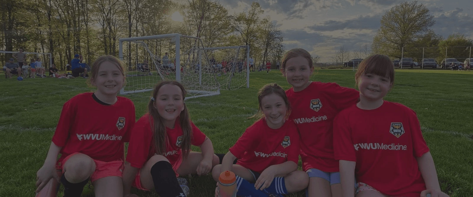 little girl teammates smiling together as sun sets on the soccer field